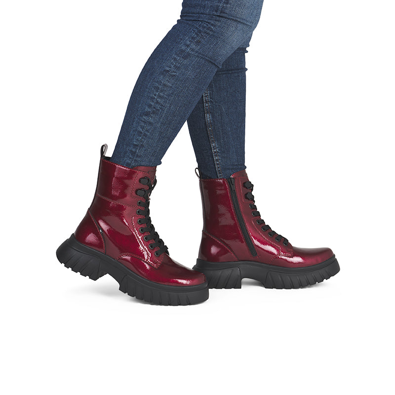 Dark red glossy leather lace-up boots with thick rubber sole, worn with jeans