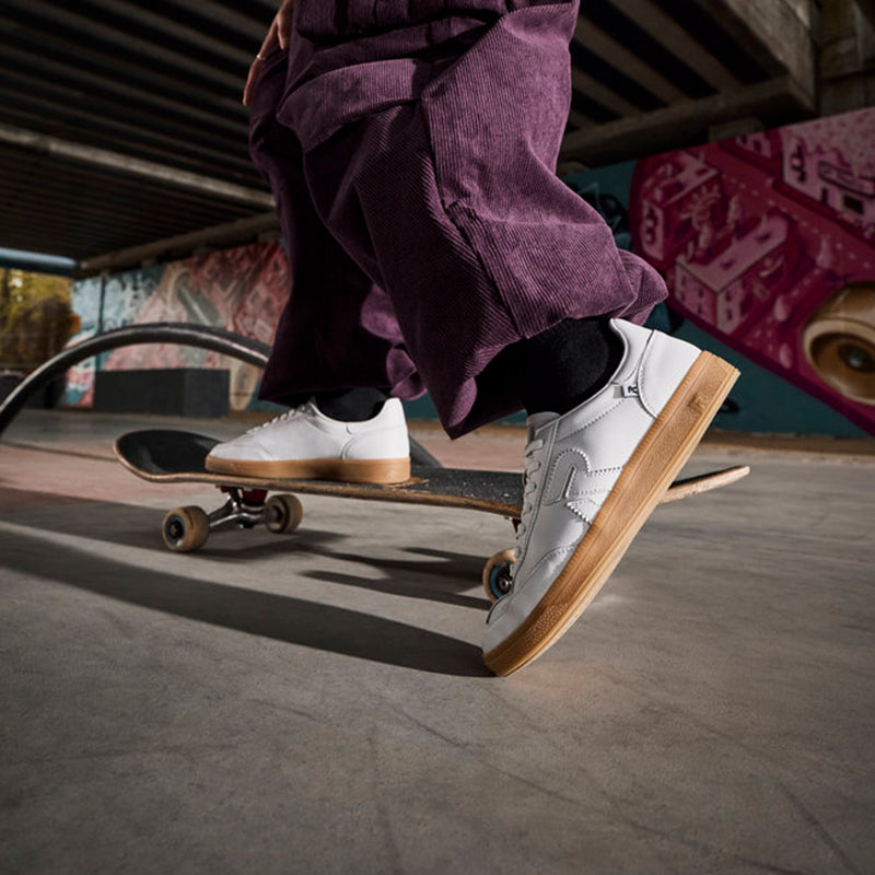 White and black lace-up sneakers with gum soles while standing on skateboard