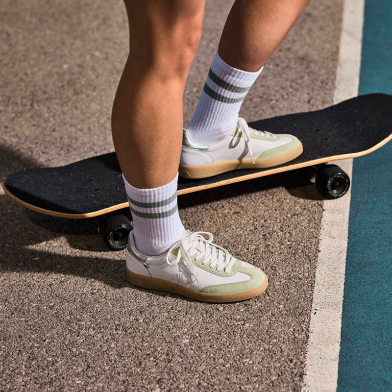 White and light green lace-up women’s sneaker on skateboard deck, with striped socks