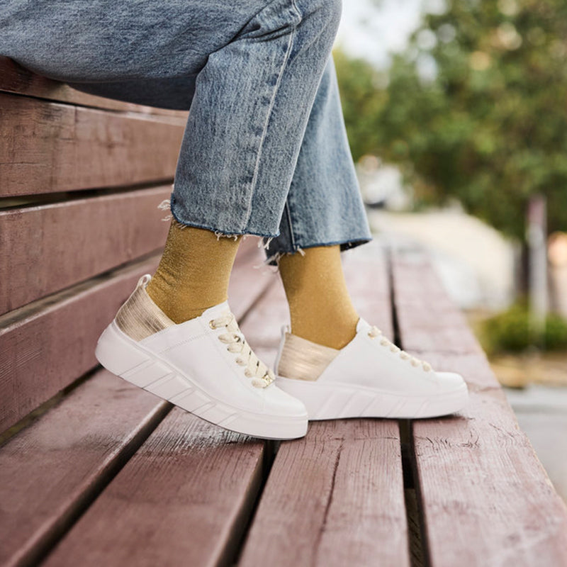 White low-top lace-up sneakers with beige socks, worn with blue jeans