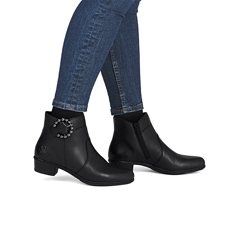 Black leather ankle boots with side zipper and jeweled ankle detail, worn with jeans.