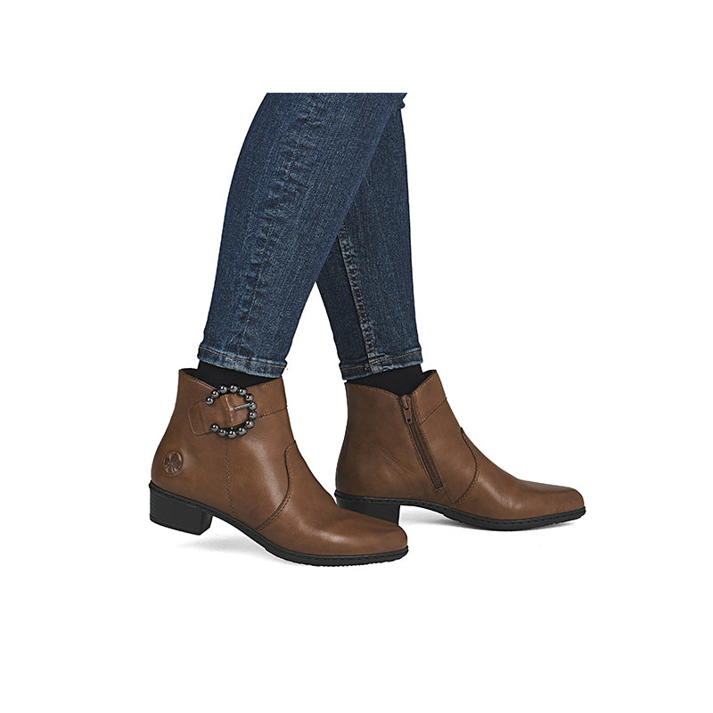 Brown leather ankle boots with side zipper and jeweled ankle detail, worn with jeans.