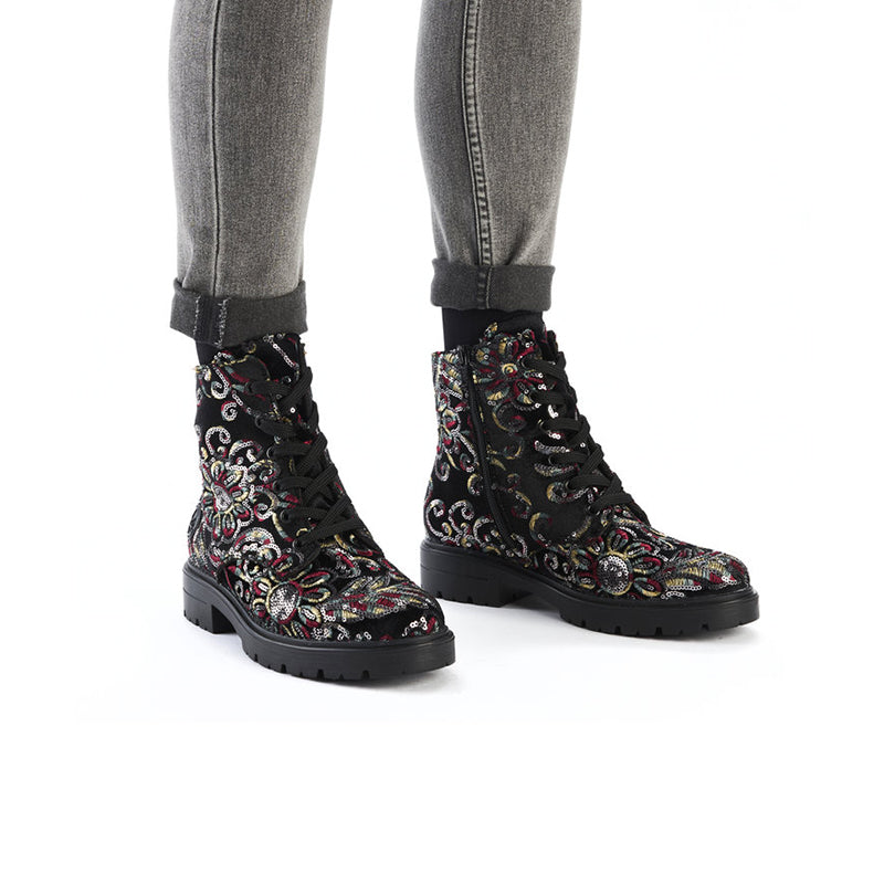 Women’s ankle boots with multicolor paisley embroidery, worn with gray jeans and socks.