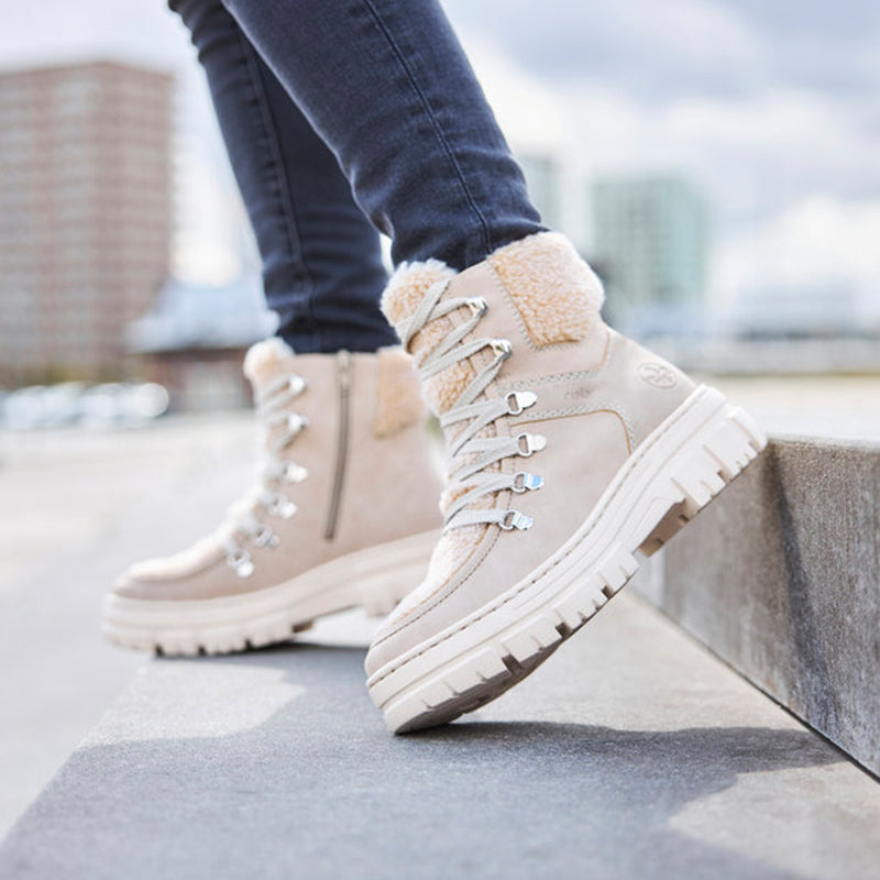Beige lace-up winter boots with thick sole and tan sherpa lining on wearer